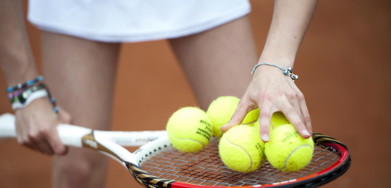 Hand greift mehrere gelbe Tennisbälle auf einem Tennisschläger, während die andere Hand die Schlägerhaltung stabilisiert.